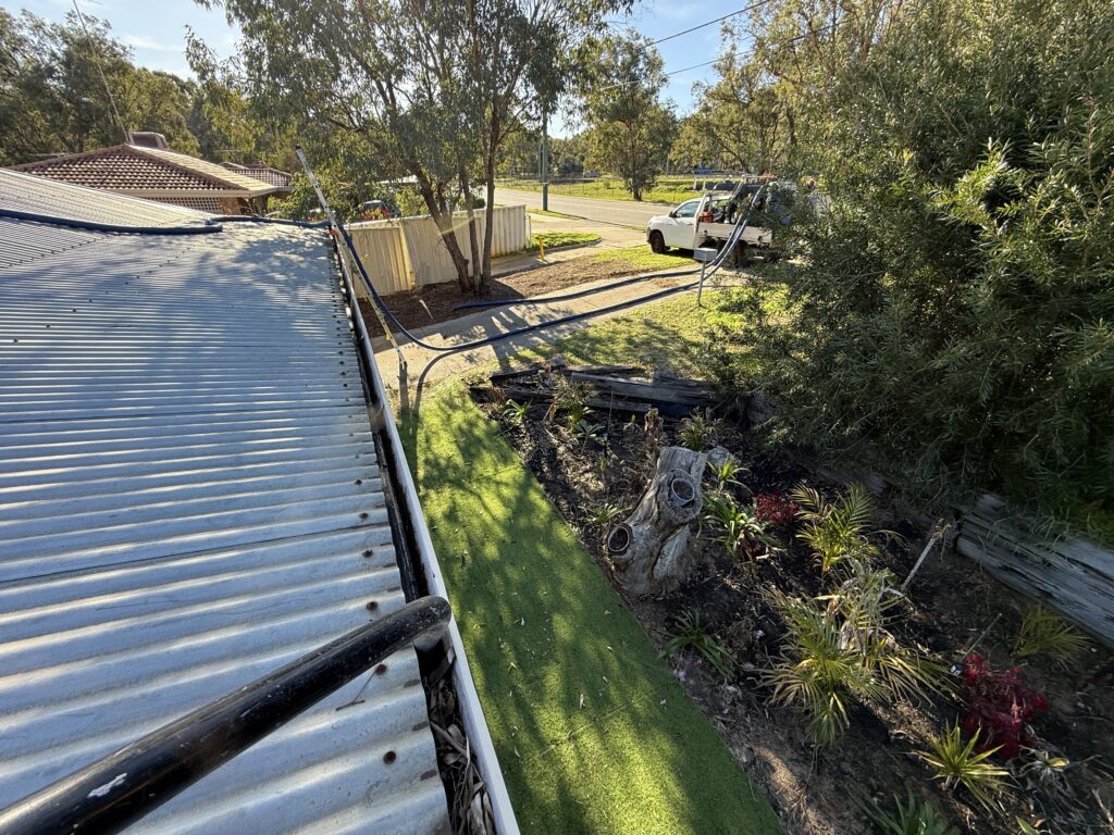Vacuum gutter cleaning in progress on a corrugated metal roof in Kalamunda