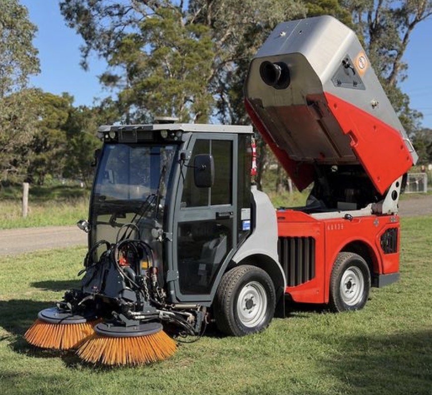 Compact street sweeper with raised hopper ready for efficient debris collection and disposal.