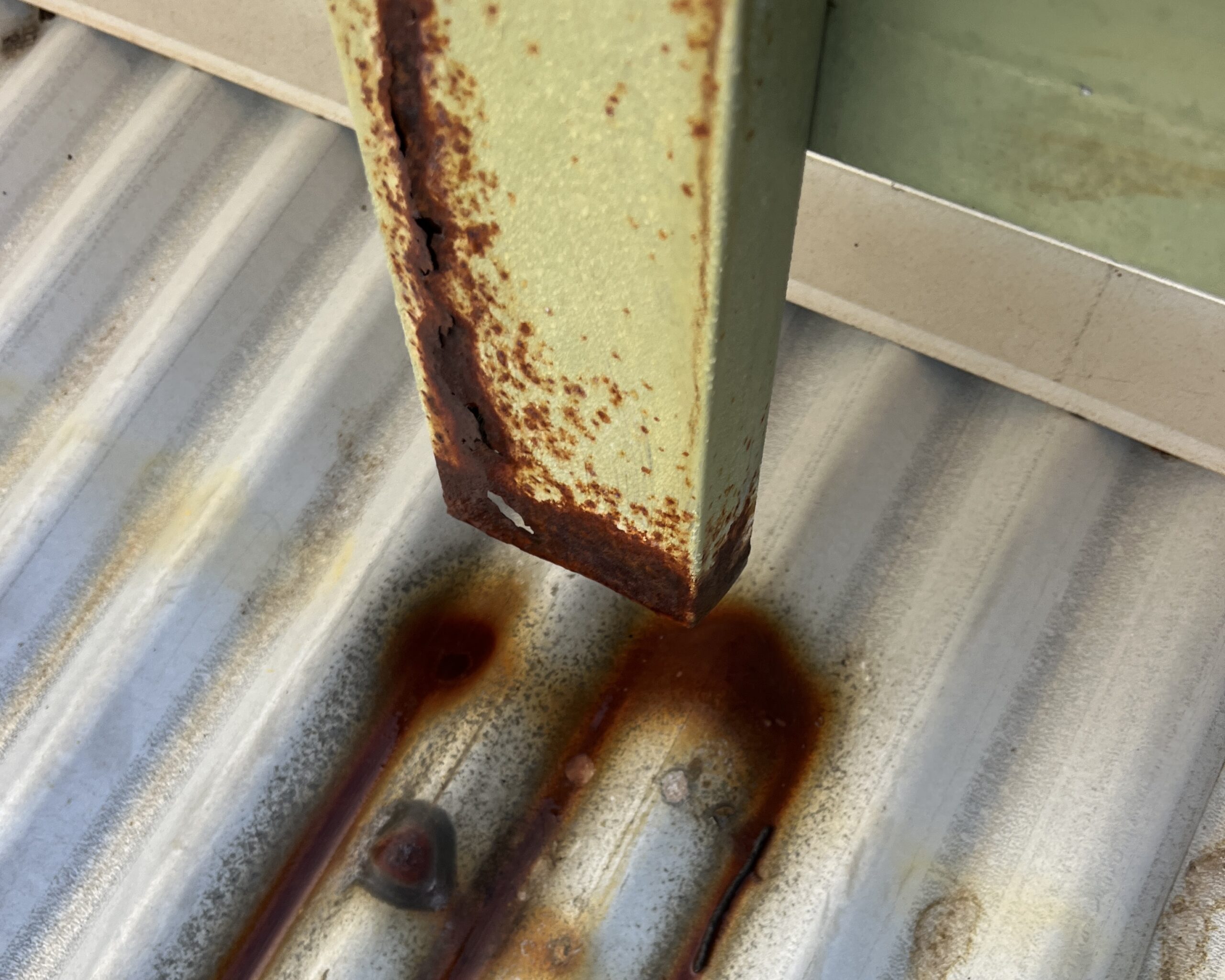 Steel downpipe showing advanced rust caused by years of acidic runoff from lichen-covered roof tiles.